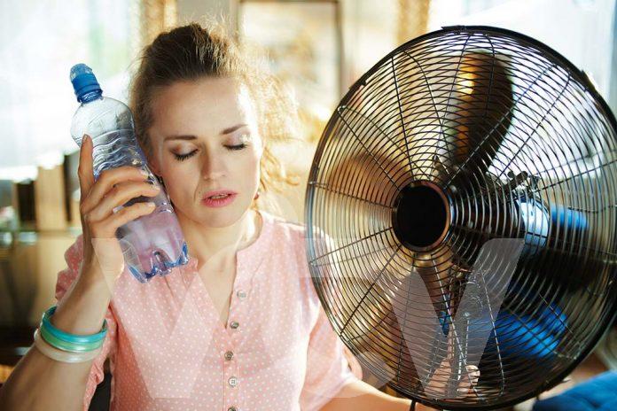 woman with bottle of water enjoying breeze in the front of fan